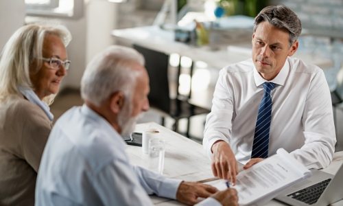 Bank manager having a meeting with senior couple and pointing at place they need to sign on the contract.